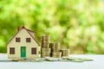 Small home model with green door and stacks of rising coins. Visual concept for a blog discussing Nevada probate laws and question s about the the Nevada Probate process.